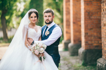 Bride and groom holding hands and walks near brick wall at wedding day. Newlyweds after wedding...