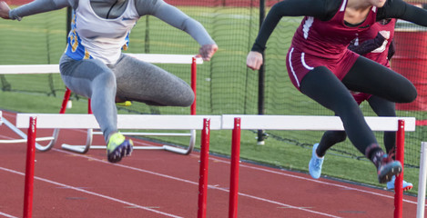 Two high school teenage girls racing in the hurdles