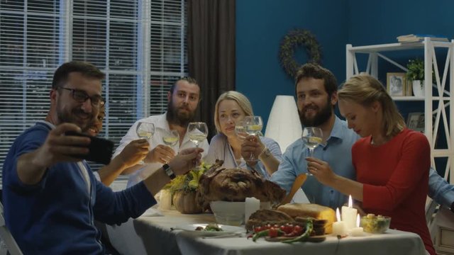 Man taking photo of diverse happy friends gathering at table on Thanksgiving day celebration and posing while having fun at home