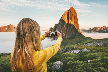 Woman blogger taking photo by smartphone exploring sunset mountains in Norway adventure trip summer...