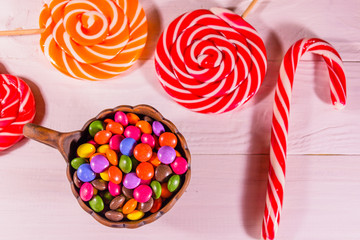 Ceramic bowl with colored candies and lollipops on a wooden table. Top view