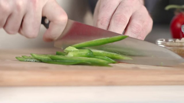 Slow-motion tracking shot of chef chopping jalapeno pepper with large kitchen knife