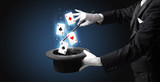 Magician with white gloves conjuring playing cards from a cylinder with magic wand