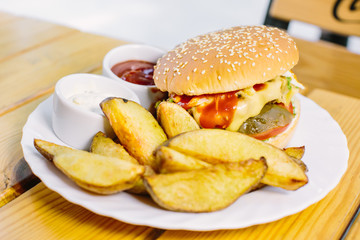 Homemade cheese burger or hamburger on wood plate served with french fries put on black granite table with copy space. Fast food for breakfast or lunch.