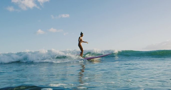 Beautiful young Hawaiian woman surfing at sunset