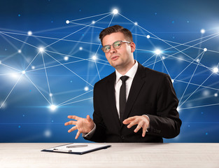 Young handsome businessman sitting at a desk with a blue connection graphic behnid him 