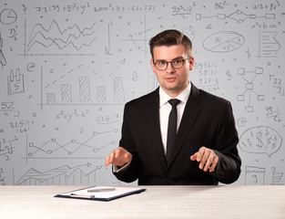 Young handsome businessman sitting at a desk with white charts behind him