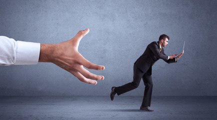Young miniature businessman running from a big hand with blueish grey background