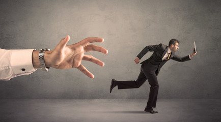 Young miniature businessman running from a big hand with grey background