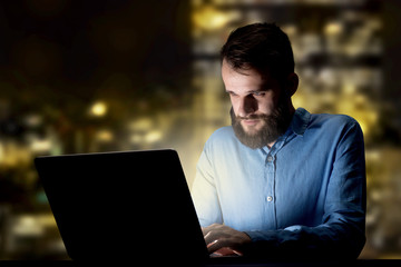 Young handsome businessman working late at night in the office with city lights in the background