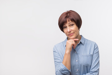 Portrait of mature confident woman in blue shirt standing on grey background