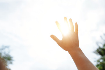 a hand reaches for the sky and covers the sun, the sun's rays make their way through the hand,...