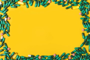 Fototapeta na wymiar Green cure pills on yellow background. Top view of medicaments