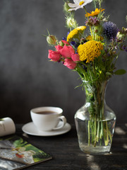 Naklejka na ściany i meble Bouquet of flowers in vase, cup of tea and magazine on wooden rustic table.
