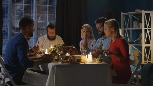 Group of diverse men and women eat and communicate while sitting at table with candles on Thanksgiving day - Powered by Adobe
