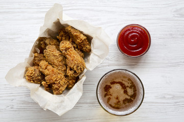 Freshly fried chicken wings with red pepper sauce, cold beer, overhead. From above, closeup.