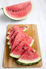 Sliced watermelon on bamboo board on a white wooden background. Side view, close-up.