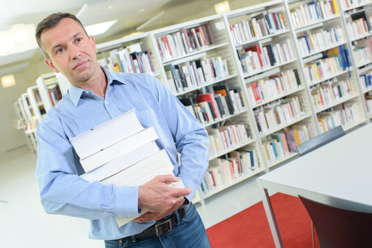 Man carrying stack of books in library