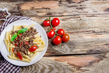 Pasta with tomatoes and meat on wooden background.