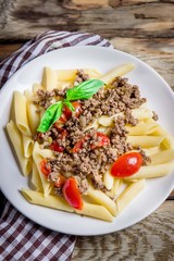 Pasta with tomatoes and meat on wooden background.