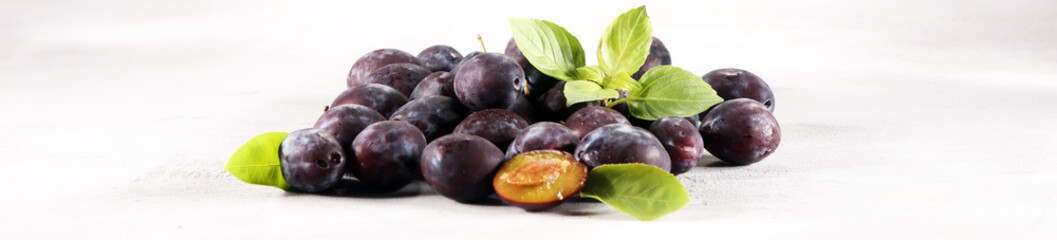 Plums on white stone background. Half of blue plum fruit. Many beautiful plums with leaves.