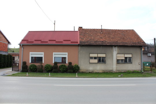 Two small attached suburban houses, one completely renovated and other dilapidated, abandoned with uncut grass and broken rusted fence