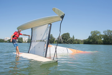 salior trying to right his catamaran after capsize