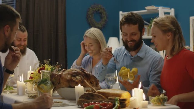 Group of diverse men and women eat and communicate while sitting at table with candles on Thanksgiving day