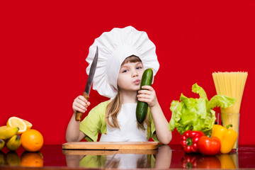 Happy little girl in chef uniform cuts vegetables in kitchen. Kid chef. Vegetarian. Cooking Process Concept