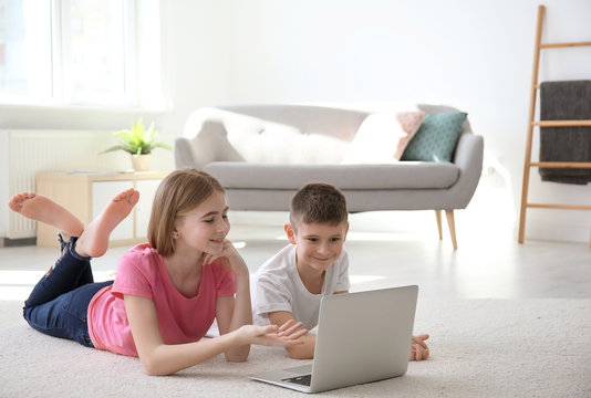 Teenage girl and her brother with laptop lying on cozy carpet at home - Powered by Adobe