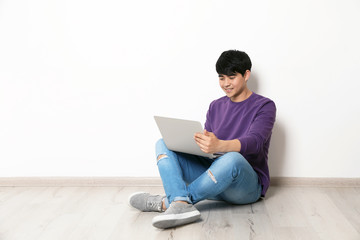 Man in casual clothes with laptop near light wall