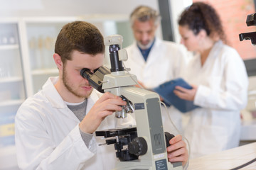 Naklejka na ściany i meble young man in protective glasses looking in microscope in laboratory