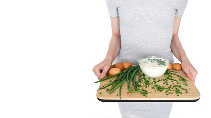 Isolated on a white background girl is holding a wooden cutting board with green onions, kifir and bun.