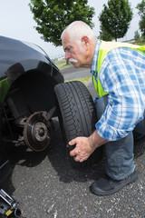 aged man changing leaking tire on the verge