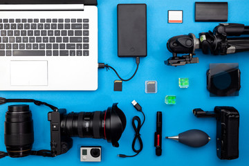 Digital camera with lenses and equipment of the professional photographer on blue paper background.