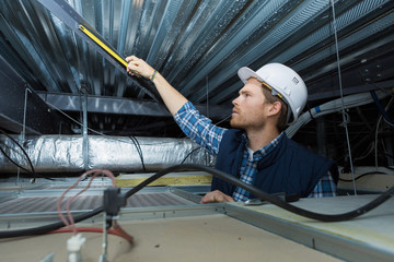 Man measuring metal bar in roof space