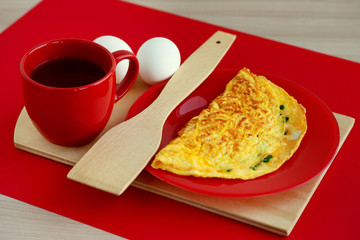 French omelette in a stylish red style. French omelette and tea on a red saucer and red background. Breakfast of eggs, grated cheese, parsley and hot black tea.