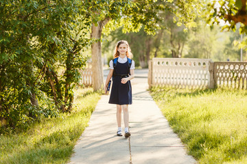 schoolgirl in uniform with a backpack and books goes to school