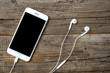 Modern smartphone with earphones on an old wooden background