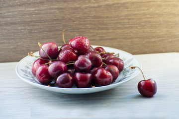 Fresh tasty cherry fruit on a plate on a wooden table. Beautiful juicy berries on a white plate.