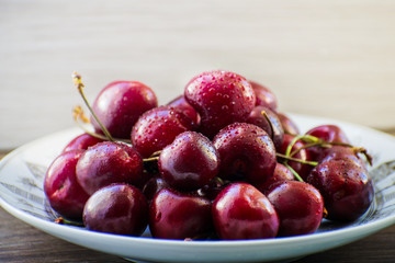 Fresh tasty cherry fruit on a plate on a wooden table. Beautiful juicy berries on a white plate.