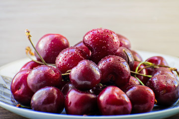 Fresh tasty cherry fruit on a plate on a wooden table. Beautiful juicy berries on a white plate.