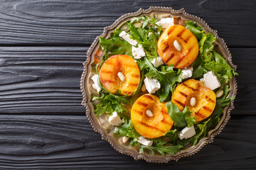 Dietary vegetarian salad with grilled peaches, with feta cheese, arugula, peanuts and herbs close-up on a plate. horizontal top view