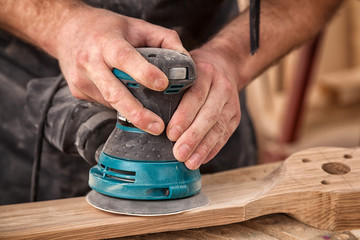 Close up of an young man builder carpenter equals polishes wooden board with a  random orbit sander...