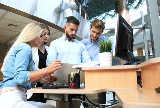 Group of young people in casual wear sitting at the office desk and discussing something while looking at PC together.