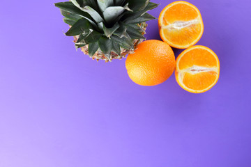 Pineapple and oranges on a purple background, citrus top view, pineapple and halves of oranges in...