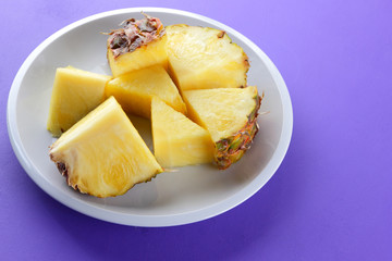 Pieces of pineapple on a white plate, chopped fresh pineapple on a violet background, salad of tropical fruits for breakfast, Mexican food