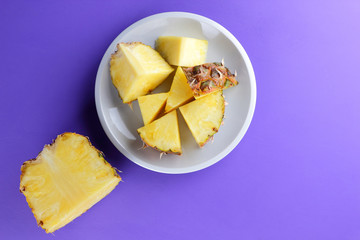 Pieces of pineapple on a white plate, chopped fresh pineapple on a violet background, salad of tropical fruits for breakfast, Mexican food