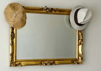 Interior view, fedora and flat cap hanging on frame of ornate gilt mirror. No-one in reflection.