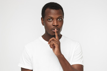 Fototapeta na wymiar Young handsome African american man isolated on gray background wearing blank white t shirt and pressing index finger to lips as if asking other to keep silent about exciting secret